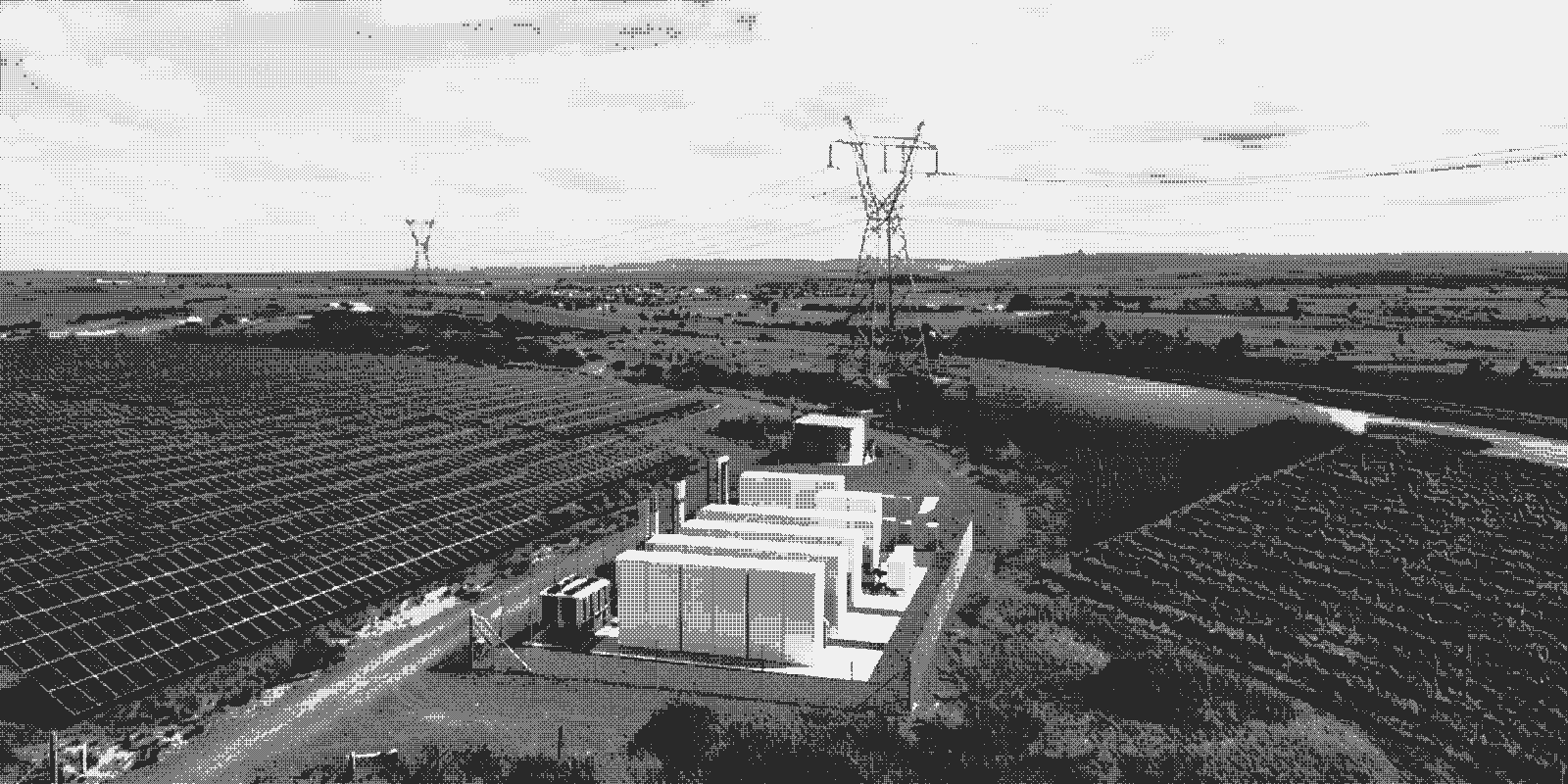 Aerial view of a generation site with a solar array, wind turbines, battery storage containers, and a transmission pylon in a single frame